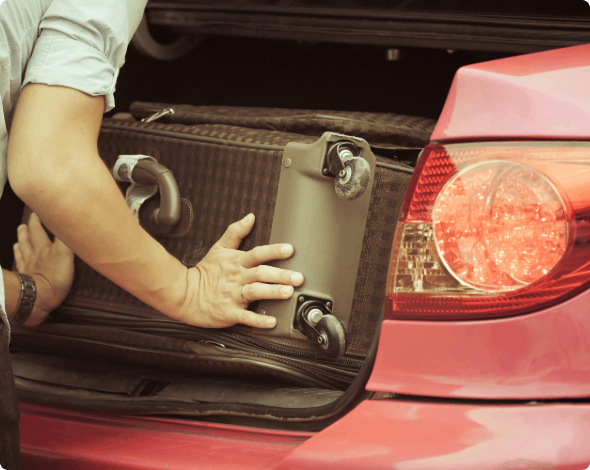 A person placing luggage in the trunk of their car.
