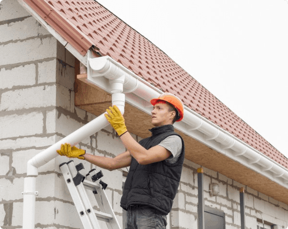 A worker affixing a downspout to a gutter on a home.