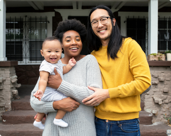 A small, happy family standing in front of a home.