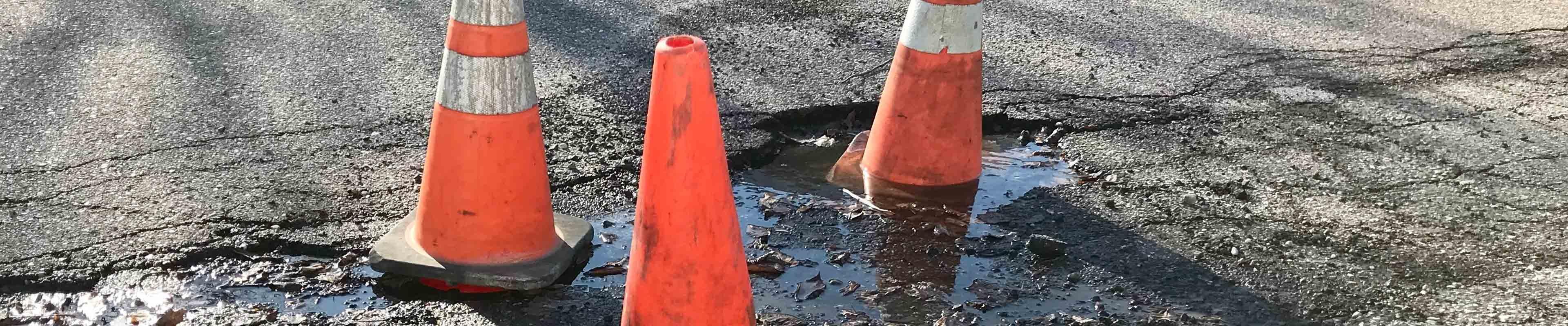 Orange cones warning cars to avoid potholes on the road.