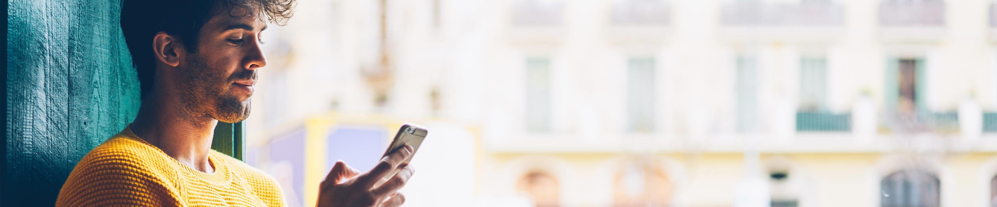 A young man in a yellow sweater uses his phone to switch car insurance companies.