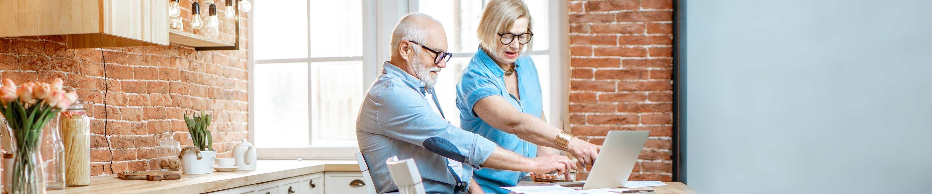 An elderly couple reviews medical expenses in their kitchen.