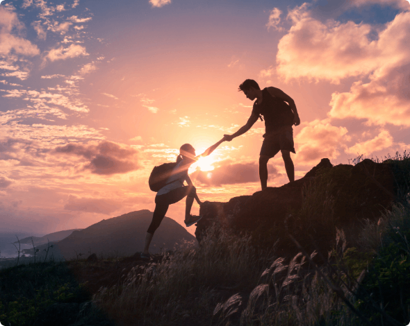 Two people climbing a mountain at sunset.