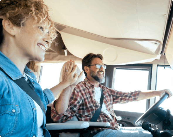 A couple giving each other a high five while going for a drive in an RV. 